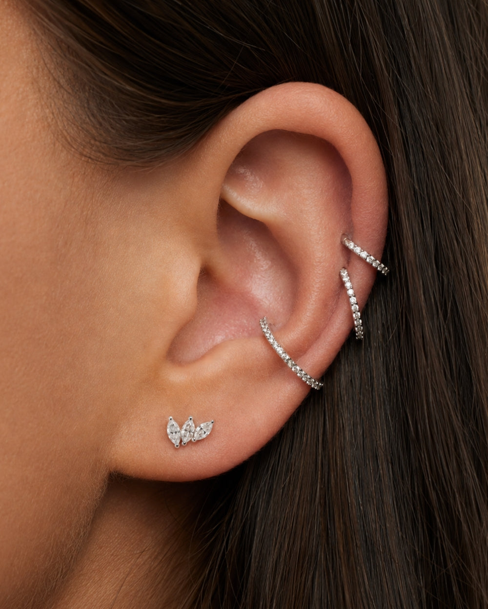 Model wearing a marquise trilogy diamond earring in a the helix of the ear with 3 ring earrings. 