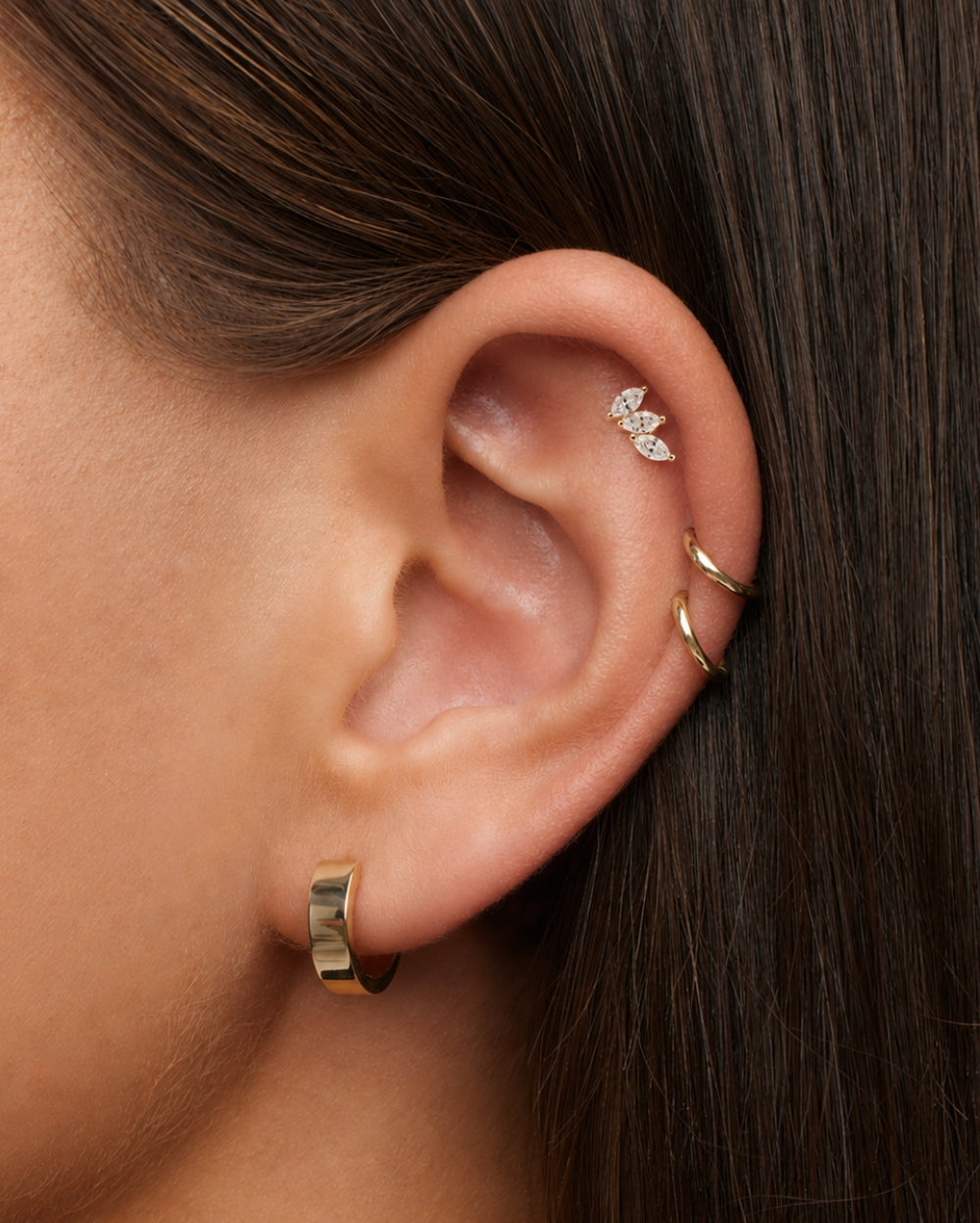 Model wearing a marquise trilogy diamond earring in a the helix of the ear with 3 ring earrings. 